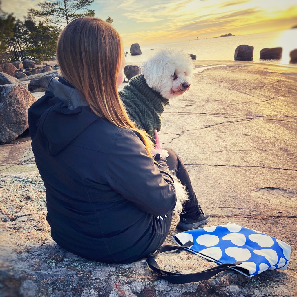 Photo of designer Sari Ahokainen with her dog Panda sitting by the ocean with a tote bag by SHALMIAK. Design: ELLIE LOVE fin.